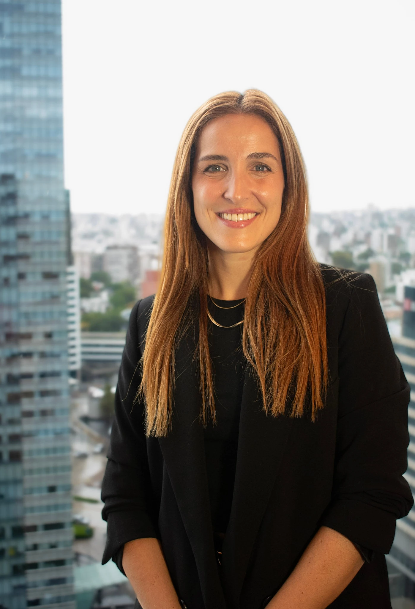 Retrato profesional de Lorena Estevez, consultora en InvestaTrust, con un fondo de edificio moderno y ventanas grandes.
