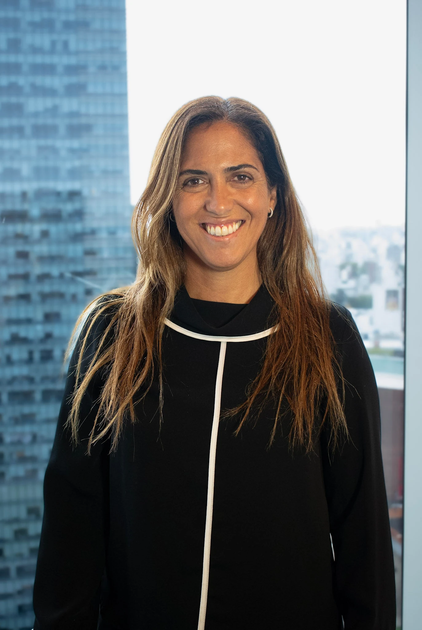 Retrato profesional de Mariana Pino, parte del equipo comercial de InvestaTrust, sonriendo frente a una ventana con vista a la ciudad.