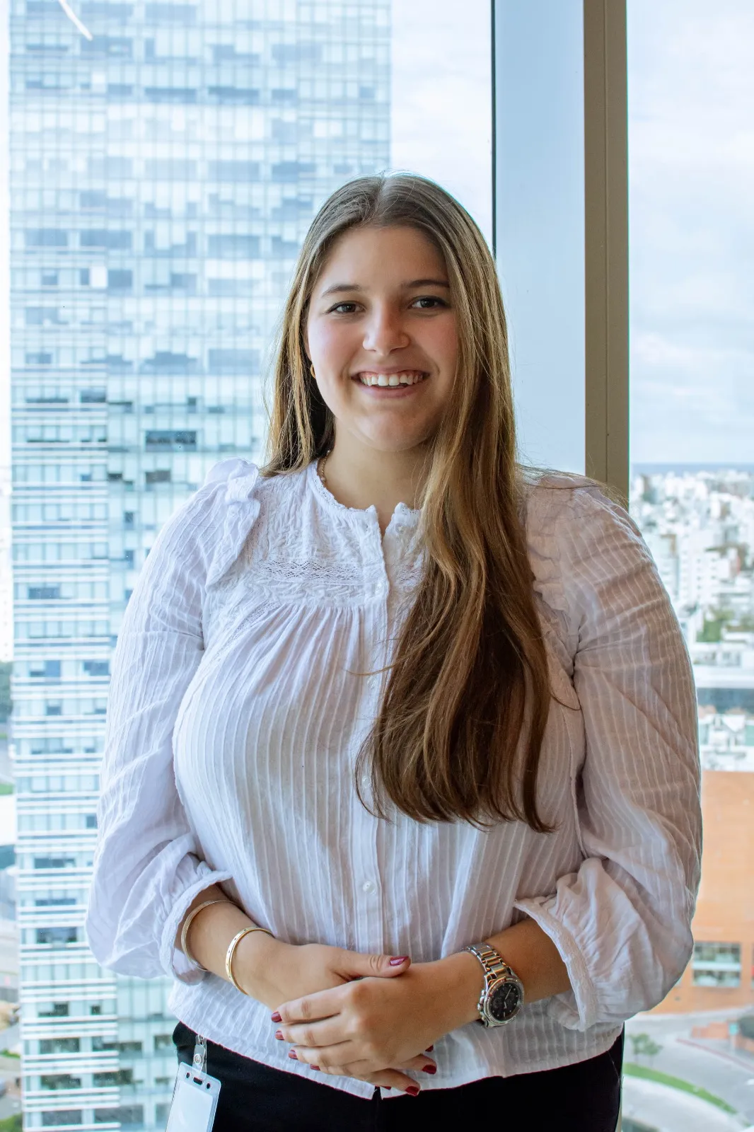 Retrato profesional de Martina Zeballos, asistente legal en InvestaTrust, posando frente a una ventana con vista a un edificio moderno en la ciudad.