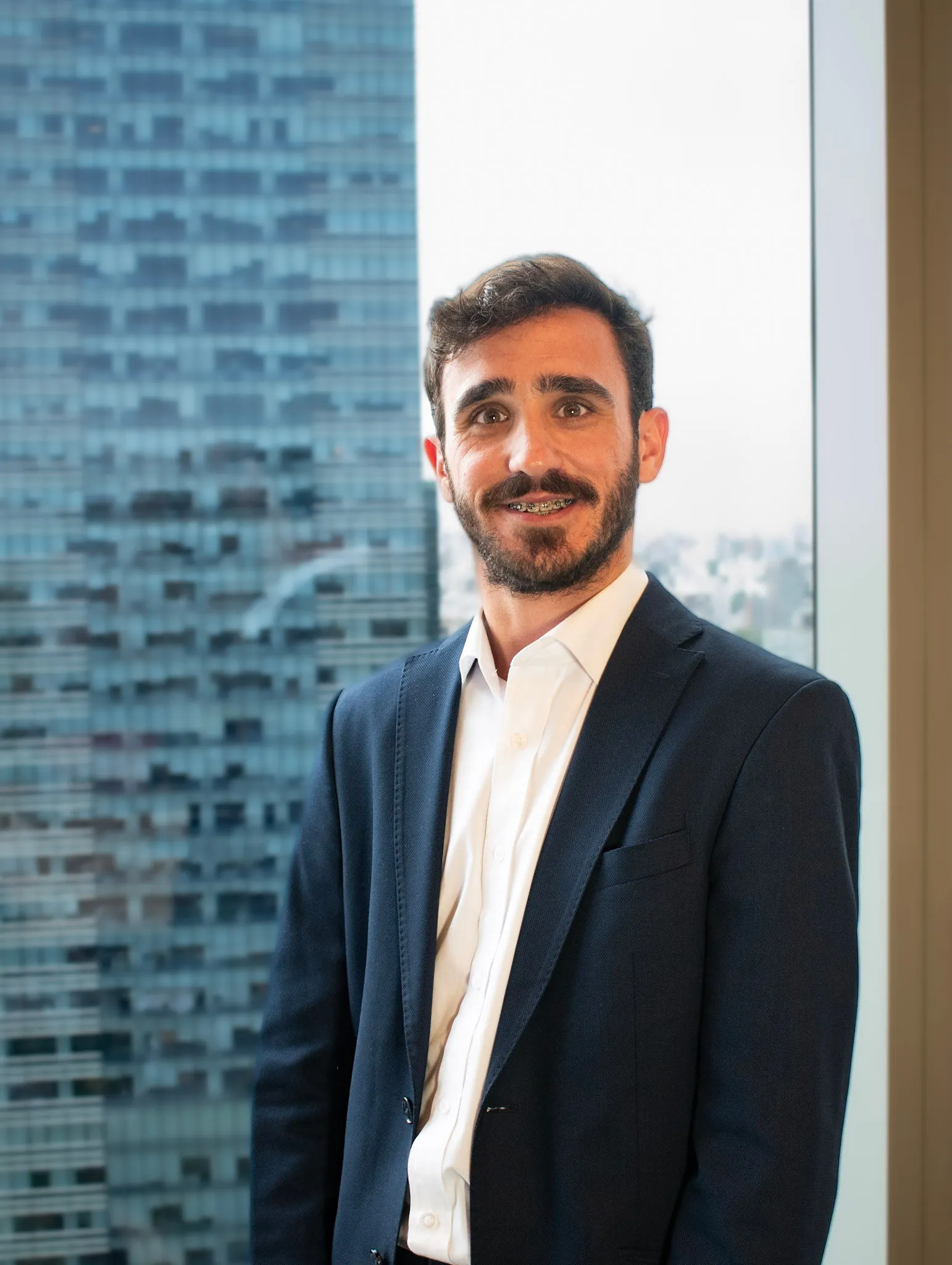 Retrato profesional de Mauricio Massanet, asistente de administración en InvestaTrust, posando frente a una ventana con vista a un edificio moderno.